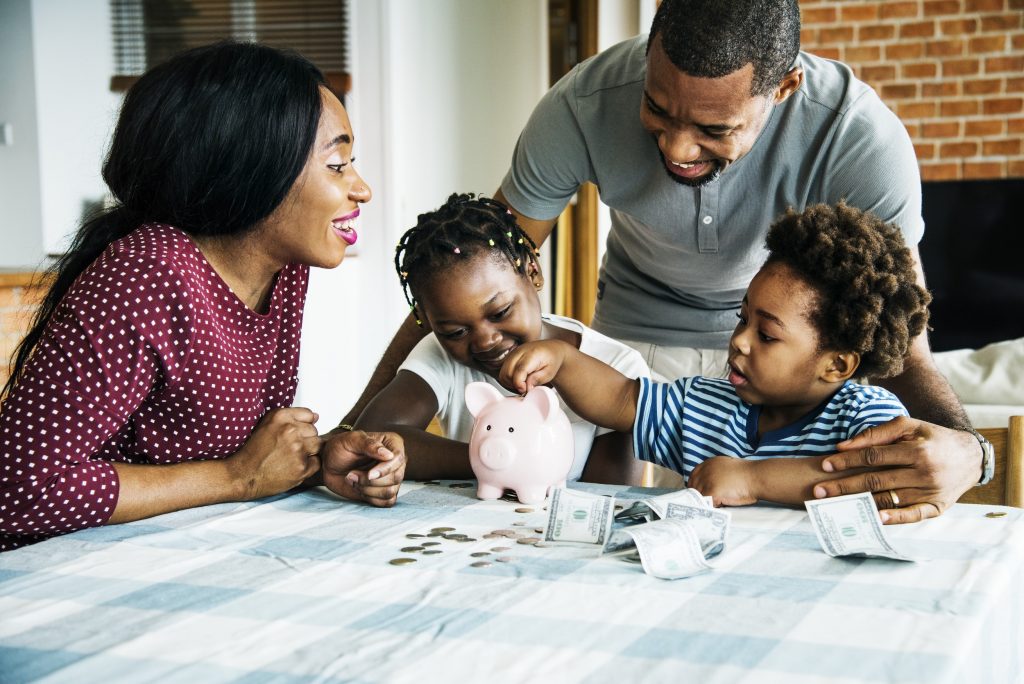 African American family counting money with the kids putting money into a piggy bank
